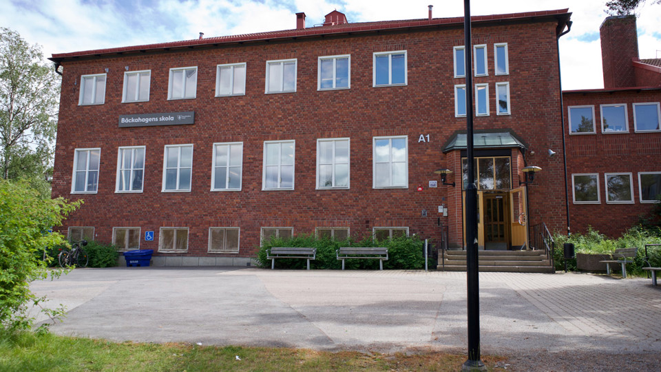 Tegelbyggnad med port, med skylt med texten Bäckahagens skola
