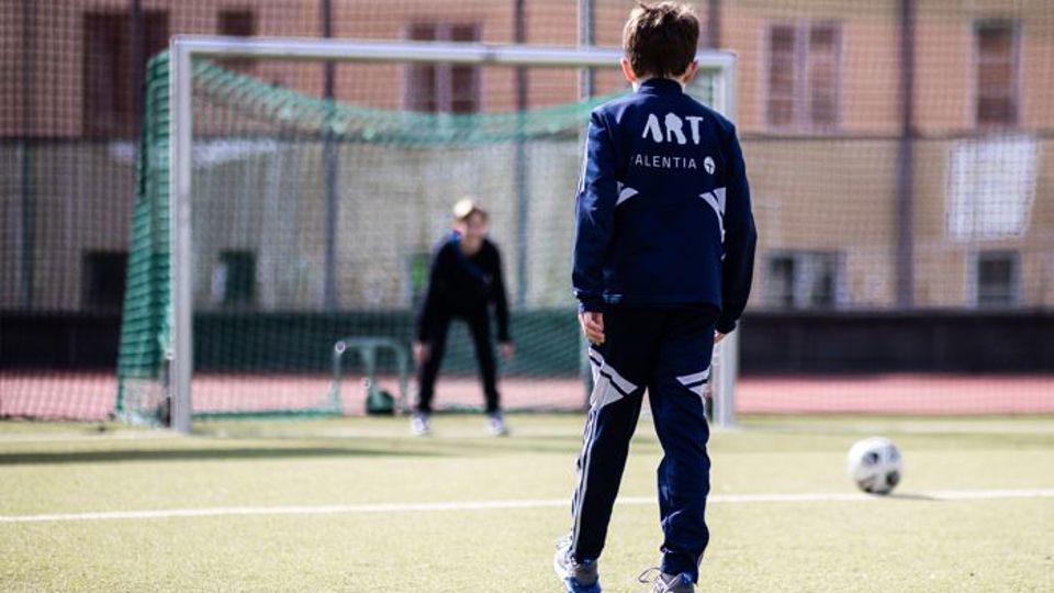 Två barn på fotbollsplan. Ett barn står beredd i mål.