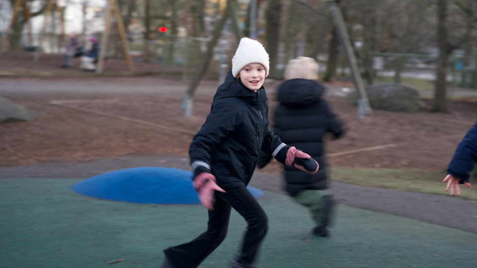 Flicka som springer över skolgård och ser glad ut