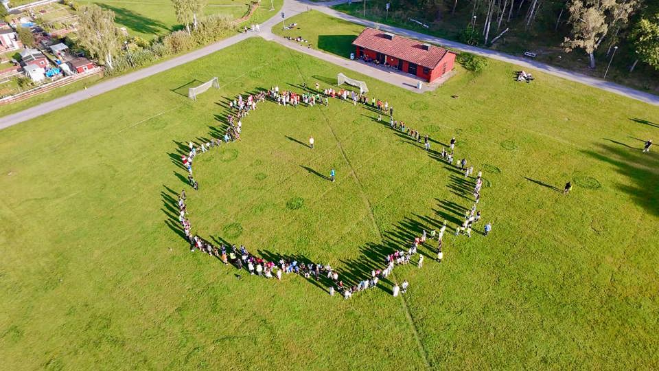 Elever står i en stor cirkel på en gräsplan vid skolan under en utomhusaktivitet.