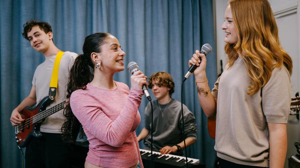 Elever sjunger och spelar instrument i en musiksal, två sjunger och andra spelar gitarr och keyboard.