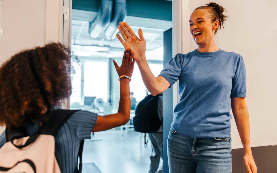 Kvinnlig lärare och elev i grundskolan gör high five med varandra