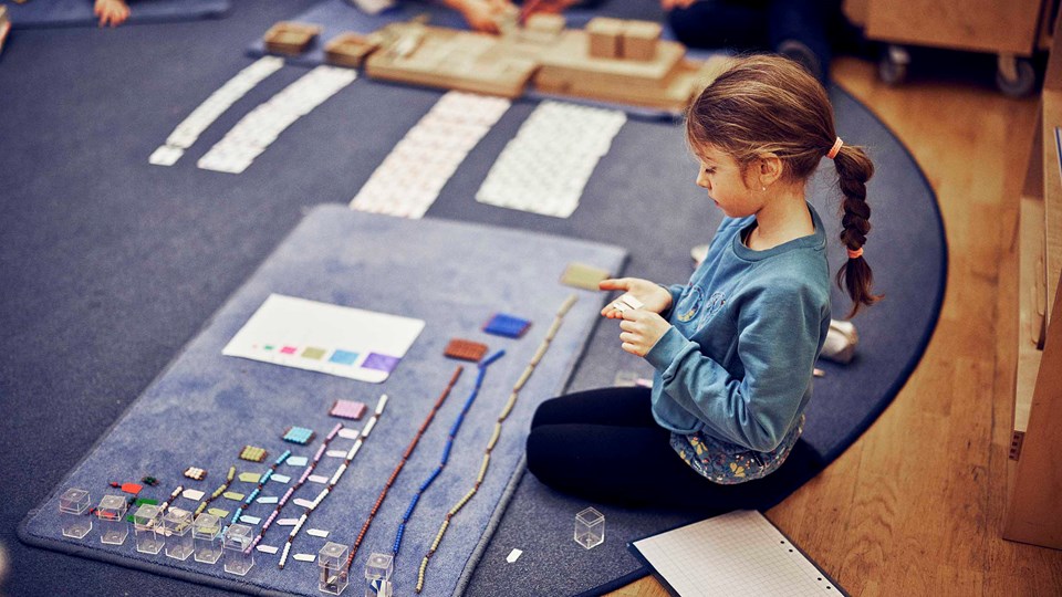 En flicka sitter på en matta och arbetar med pärlor i olika färger och former.