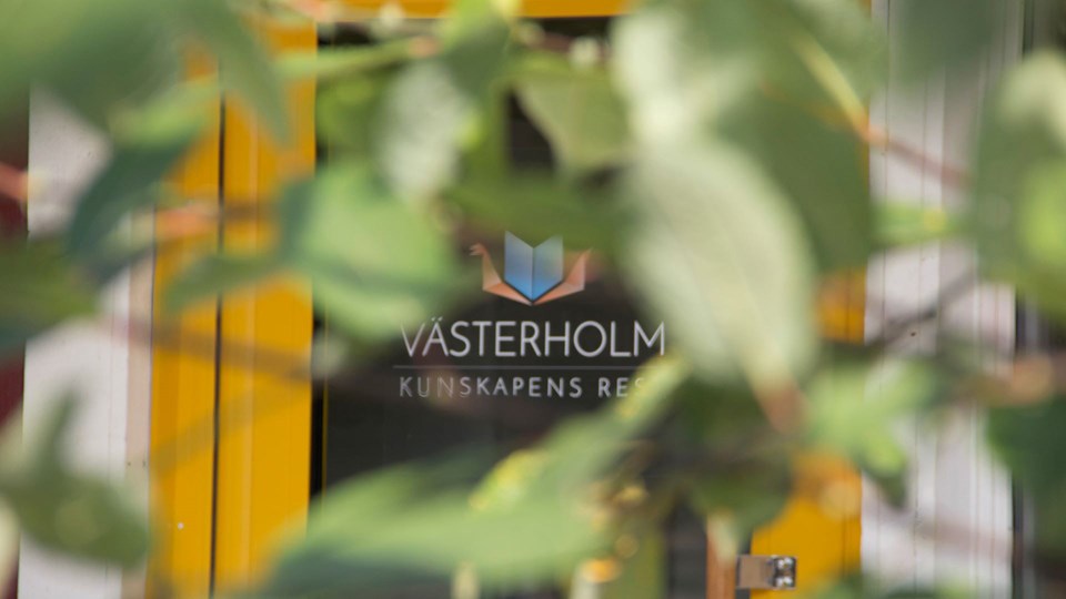 En gul entrédörr med glasfönster. På dörren står det Västerholm kunskapens resa.