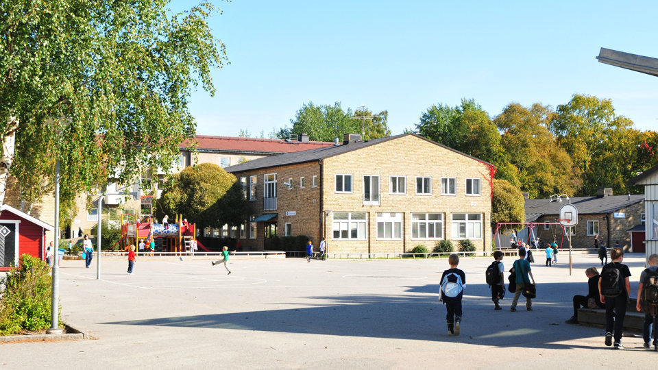 Tallkrogens skola, ett tvåvåningshus i gult tegel. På skolgården framför skolan leker, spelar fotboll och umgås barn.